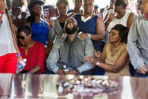 Black man, head thrown back and wailing in grief as family and loved ones try to console a father's grief.  